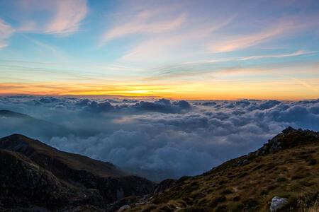 A russet hillside that looks out over clouds and a yellow sunset beneath a light blue sky.