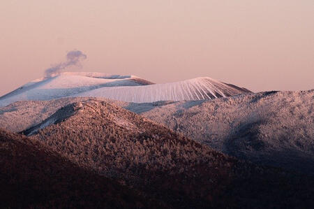 A pink-tinted image of a volcanic mountain range sprinkled with dust and snow.
